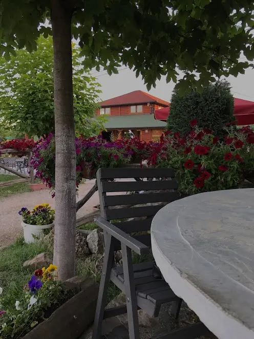 Red and pink flowers around a stone table in the garden, a red-roofed house behind