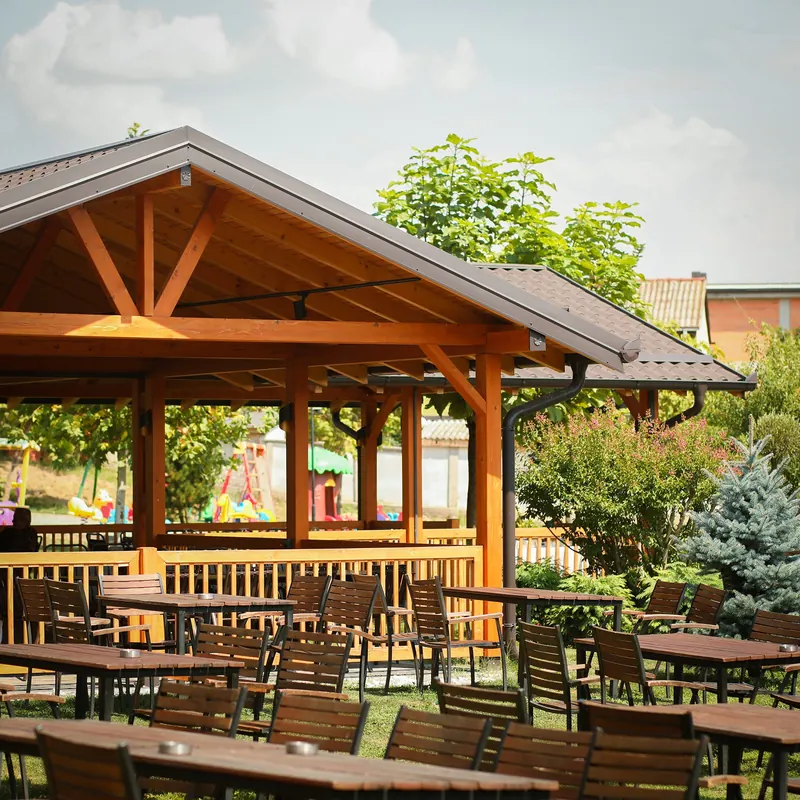 The garden of Restaurant Bifurkacioni with a wooden pavilion, tables on the lawn and blue spruce trees
