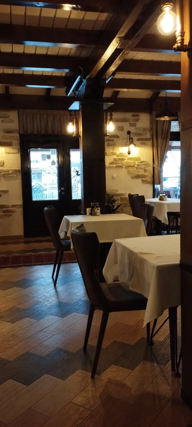 A tall view of the dining room with wooden pillars, lamps and patterned floor tiles