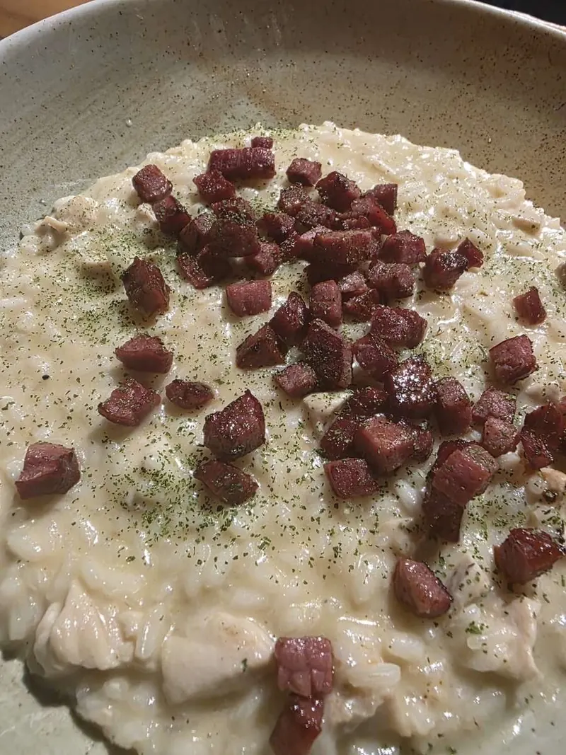 A plate of creamy risotto topped with small pieces of cured meat