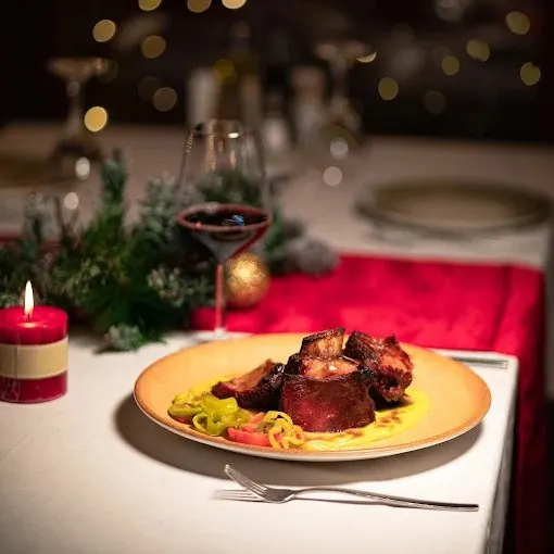Slow-cooked meat with peppers on a plate, a glass of red wine behind