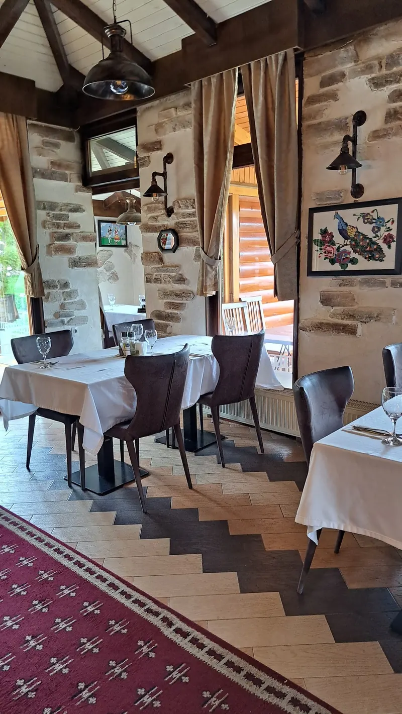 A dining room with stone walls, curtains, a red carpet and tables set with white cloths